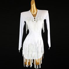 a white flap dress with fringes and beads on the skirt is displayed in front of a black background