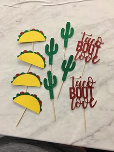 three taco bout cake toppers on a marble table with the words taco bout spelled in red, yellow and green