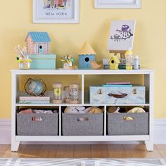 a white shelf with baskets on top of it in front of a yellow painted wall