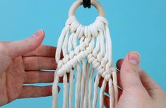 two hands are holding a piece of white yarn that is hanging from a hook on a blue background