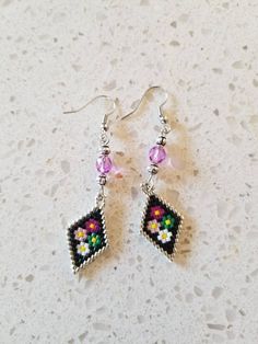 a pair of earrings with beaded designs on them sitting on a white table top