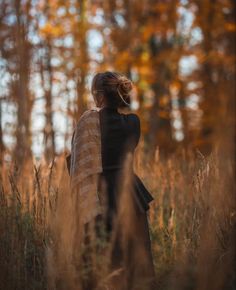 a woman standing in tall grass with her back to the camera and looking at trees