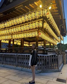 a woman standing in front of a building with lanterns hanging from it's roof