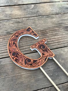 the letter c is made out of wood and has an intricate design on it, along with two toothpicks