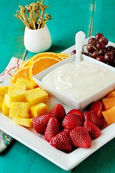 a plate topped with fruit and dip surrounded by oranges, grapes, strawberries