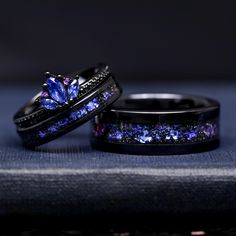 two wedding rings with purple and blue crystals on them, sitting next to each other