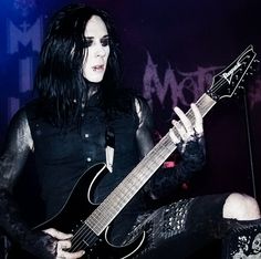 a man with long black hair playing an electric guitar