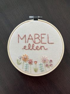 a close up of a embroidery on a piece of wood with the words mabel ellen written in red