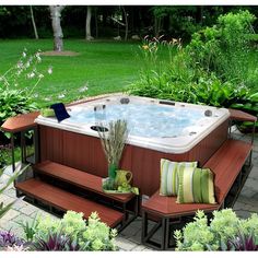 a hot tub surrounded by wooden benches and plants in a yard with flowers on the side