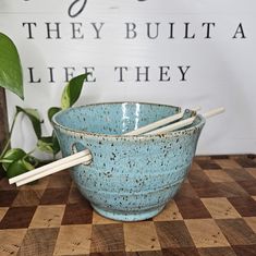 a blue bowl with chopsticks in it sitting on a checkered table