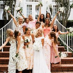 a group of women standing next to each other in front of a white house holding bouquets