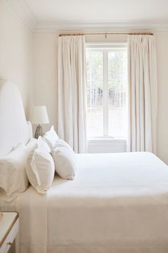 a white bed sitting next to a window in a room with curtains on the windowsill