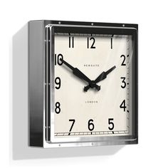 a square clock with black hands and numbers on the face is hanging from a wall