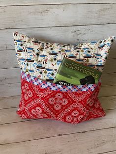 a red and white pillow sitting on top of a wooden floor next to a book