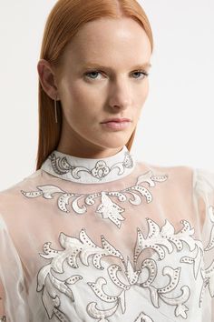 a woman with long red hair wearing a white dress and silver jewelry on her neck