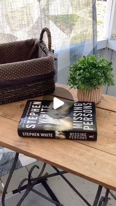 a book sitting on top of a wooden table next to a basket filled with plants