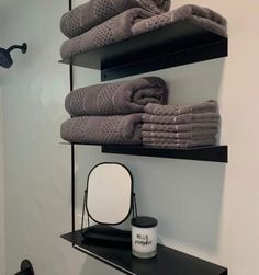 towels are stacked on shelves in the bathroom, with a mirror and candle beside them