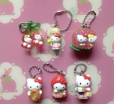 hello kitty keychains are laying on a pink surface with flowers and leaves in the background