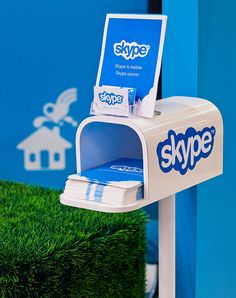 a skype mailbox sitting on top of a lush green field next to a blue wall