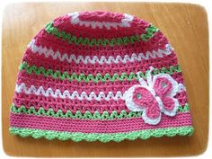 a crocheted pink and green hat with a flower on it sitting on a wooden table