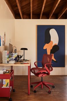 a red chair sitting in front of a desk with a painting on the wall behind it