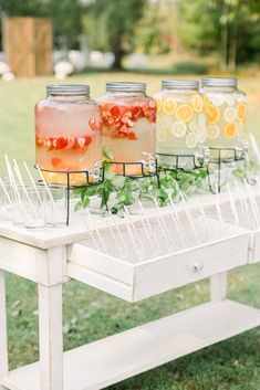 three jars filled with liquid sitting on top of a white table covered in leaves and flowers