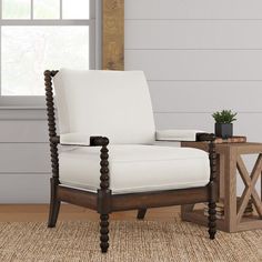 a white chair sitting in front of a window next to a table with a potted plant on it