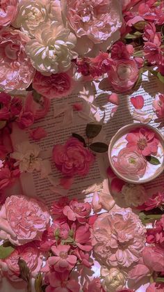 some pink flowers are laying on top of an open book and next to a bowl