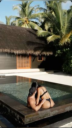 a woman in a bathing suit sitting on the edge of a pool next to a hut