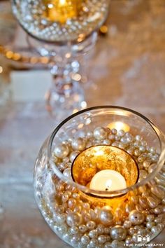 two wine glasses filled with pearls and a candle on top of a white table cloth