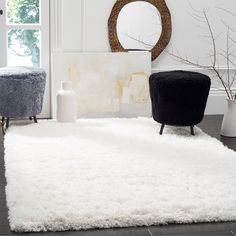 a living room with white rugs and black chairs in the corner next to a round mirror