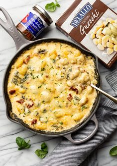 an iron skillet filled with cheese and spinach on top of a marble counter