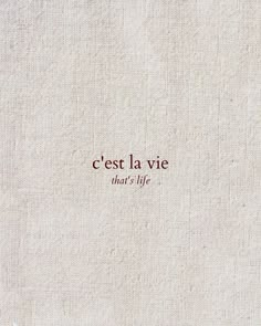 the words cest la vie written in red ink on a white linen textured background