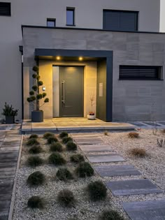 the front entrance to a modern home with gravel and plants on the ground in front of it