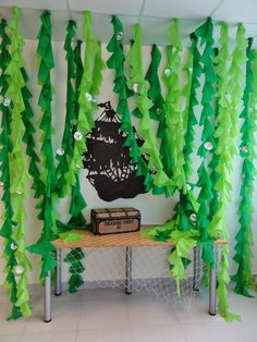 a room decorated with green streamers and paper trees on the wall, along with a black pirate ship