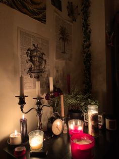 several candles are lit on a table in a dark room with pictures and greenery