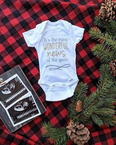 a baby's bodysuit and pine cones on a plaid blanket with the words it's the most wonderful news of the year