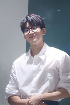 a young man wearing glasses standing in front of a green wall with his hands on his hips