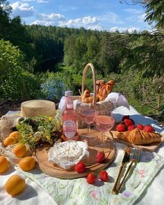 an outdoor picnic with fruit, cheese and bread on the table in front of trees