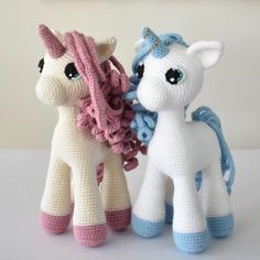 two crocheted unicorns standing next to each other on a white table top