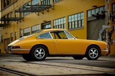 an old yellow porsche parked in front of a building