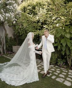 the bride and groom are walking through the garden holding each other's hands as they look at each other