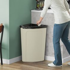 a woman standing next to a trash can in a room with green walls and wooden flooring