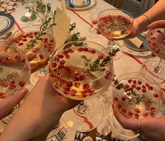 several people holding wine glasses filled with liquid and garnished with greenery on the table