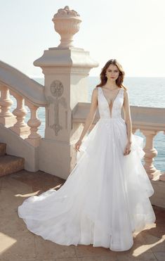 a woman in a white wedding dress standing on the stairs by the ocean with her hand on her hip