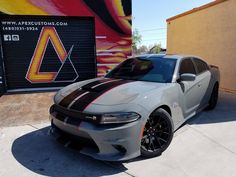 a gray and black dodge charger parked in front of a building with graffiti on it