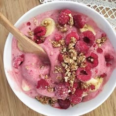 a bowl of ice cream with raspberries and granola on top, next to a wooden spoon