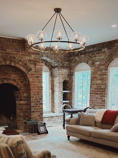 a living room filled with furniture and a fire place under a chandelier in front of two windows