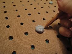 a person is holding a pencil and pointing to a golf ball on a table with holes in it