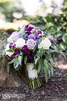 a bouquet of purple and white flowers sitting on top of a tree stump in the woods